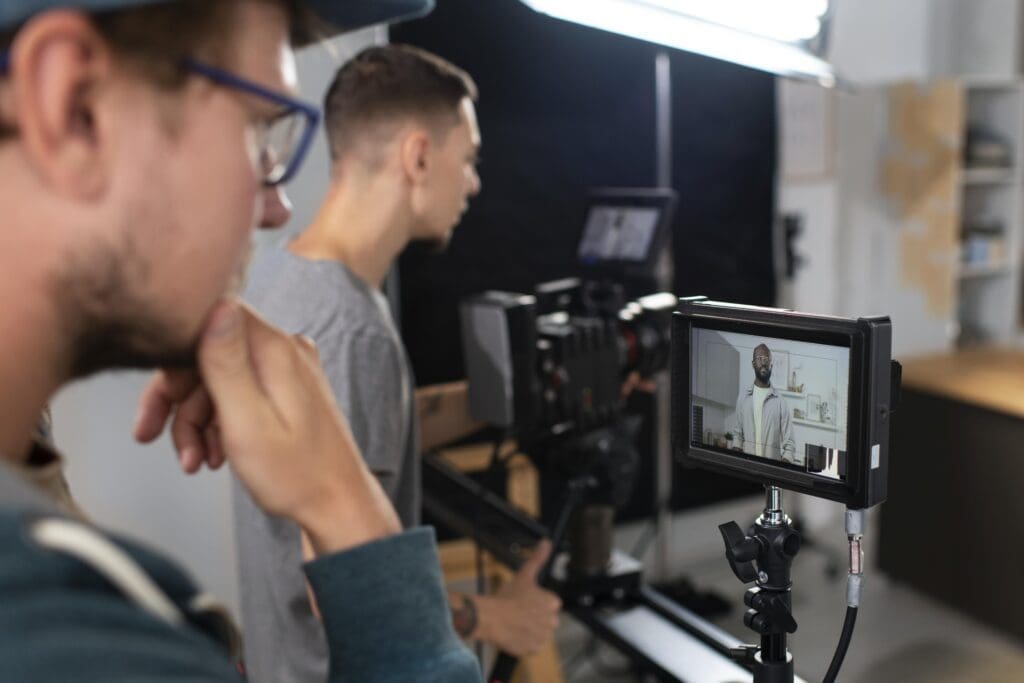 Scale With Video Two men operate a camera and monitor during a video shoot in Texas, with one subject visible on the monitor screen talking. This setup showcases how business owners can scale with video through effective content creation. Texas